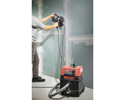 Un bărbat șlefuiește un perete cu o mașină de șlefuit gips-carton conectată la un aspirator.