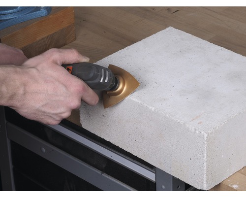 O persoană taie o piatră de beton cu o unealtă multifuncțională.