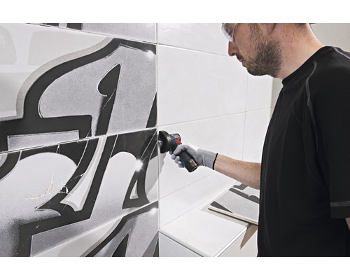 Un meșter lucrează la plăci ceramice cu un polizor unghiular într-o baie.