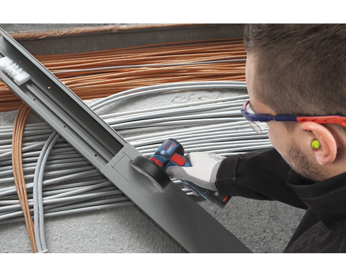 Electrician prelucrează canalul de cablu cu un instrument multifuncțional în fața cablurilor