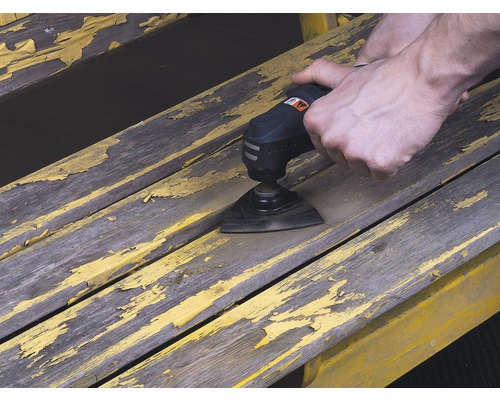 O persoană folosește un instrument multifuncțional pentru a șlefui vopseaua de pe o bancă de lemn.