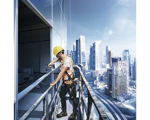 Un muncitor în construcții cu cască și vestă de protecție montează ferestre la o clădire la înălțime