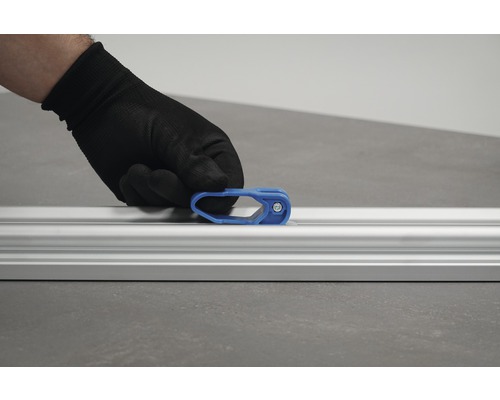 O mână cu mănușă de protecție fixează un glisor albastru pe o șină de aluminiu.