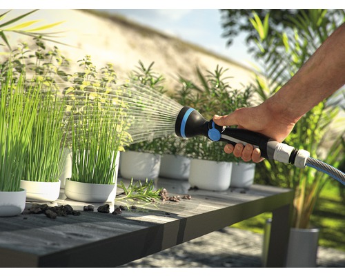 O persoană udă plante în ghivece cu un pulverizator de grădină pe o masă.