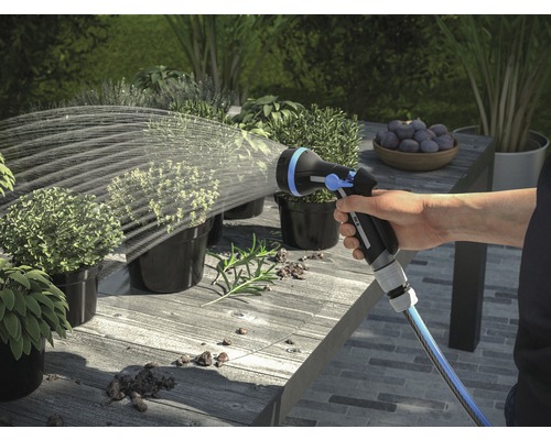 O mână udă plante cu un pulverizator de grădină pe o masă afară.