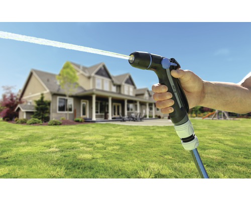 Pistol de stropit pentru grădină cu jet de apă și casă în fundal