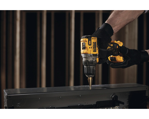 Sigla DeWalt. O persoană găurește o carcasă metalică cu o mașină de găurit.