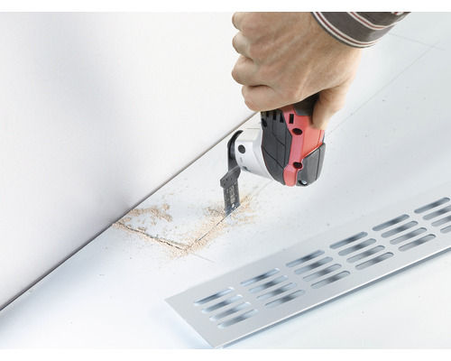 O persoană taie cu o unealtă multifuncțională o fâșie într-o podea pentru un radiator.