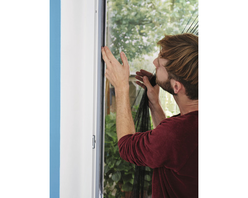 Bărbat atașând o plasă de țânțari de un toc de fereastră.