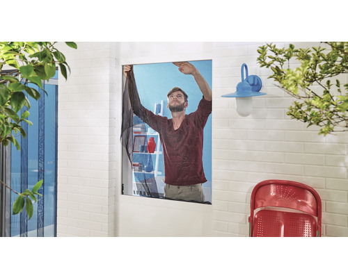 Un bărbat montează o plasă de insecte pe o fereastră.