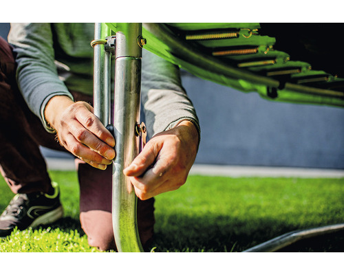 Persoană care asamblează o trambulină de grădină cu arcuri și cadru metalic.