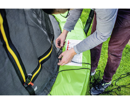 Un bărbat asamblează o trambulină de grădină cu plasă de siguranță.