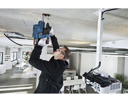 Un bărbat găurește un orificiu în tavan într-un birou cu o mașină de găurit