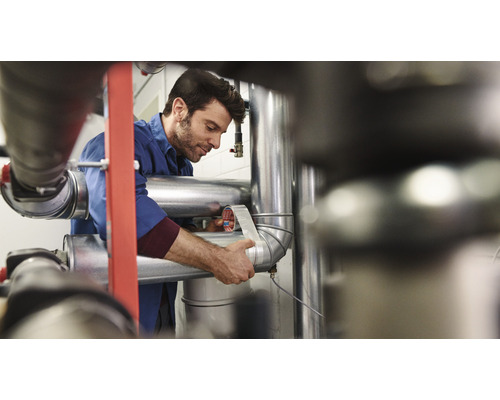 Un bărbat înfășoară o conductă cu bandă de etanșare.