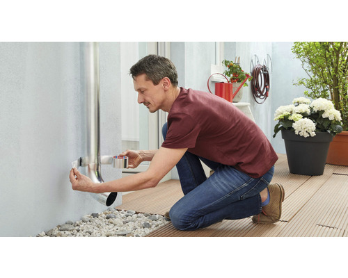 Un bărbat fixează o țeavă de ploaie de un perete de casă cu bandă de etanșare.