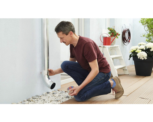 Un bărbat fixează o conductă de ploaie pe un perete exterior al unei case.