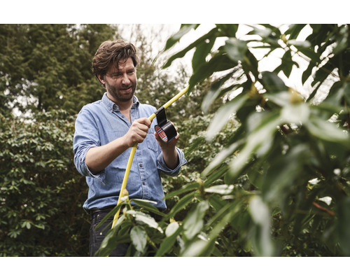 Bărbat reparând un furtun galben cu bandă adezivă neagră în grădină.