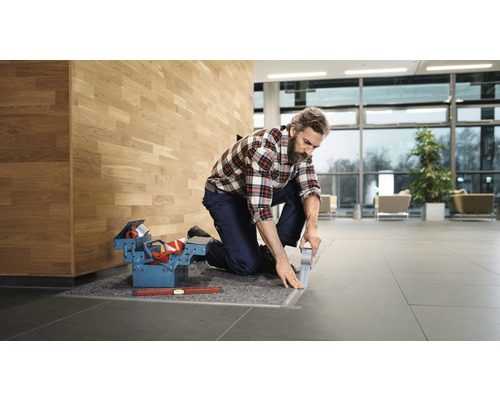 Artizan îngenuncheat cu cutie de scule și bandă adezivă pe podea