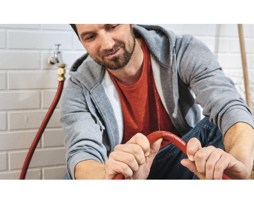 Bărbat ține un furtun de apă cu scurgeri.