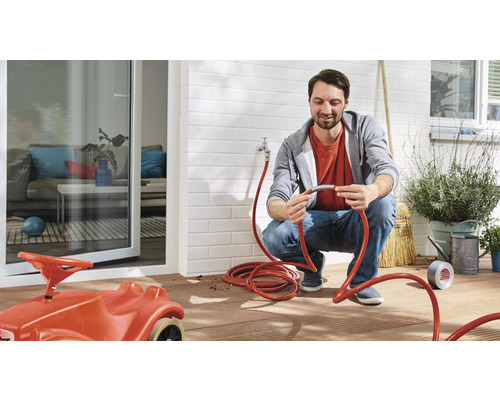 Bărbat conectează un furtun de grădină în exterior, cu o mașină de jucărie pentru copii în prim-plan