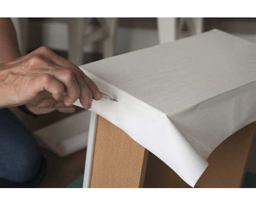 Persoană care taie folie pe o piesă de mobilier cu un cuțit hobby.