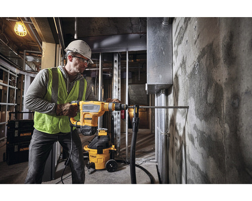Un bărbat găurește un perete de beton cu un ciocan rotopercutor DeWalt.