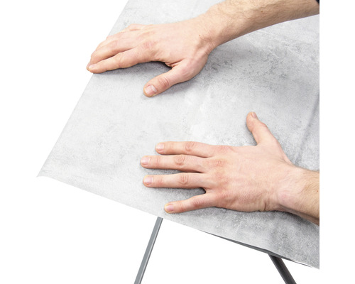 Bărbat care fixează folie de mobilă pe o suprafață.