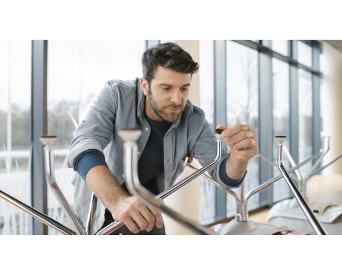 Un bărbat asamblează o masă cu picioare metalice și protecții pentru podea