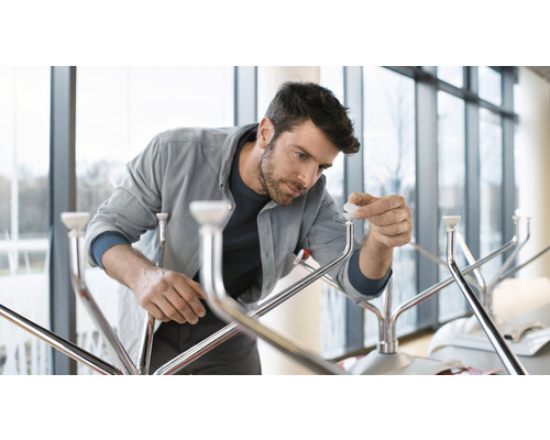 Un bărbat asamblează un suport pentru haine cu finisaj metalic și capace terminale albe.