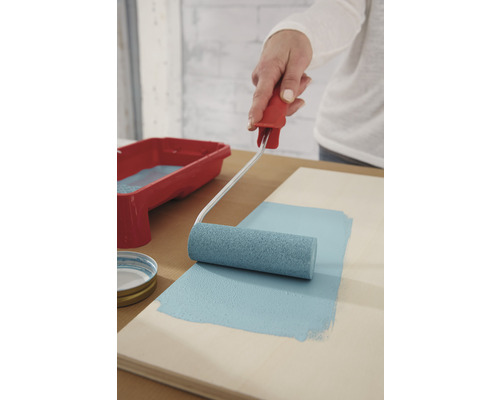 Persoană care vopsește o scândură de lemn cu trafalet și vopsea albastră