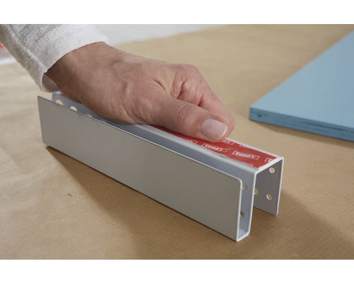 O mână ține o bandă de profil argintie cu bandă adezivă dublă.