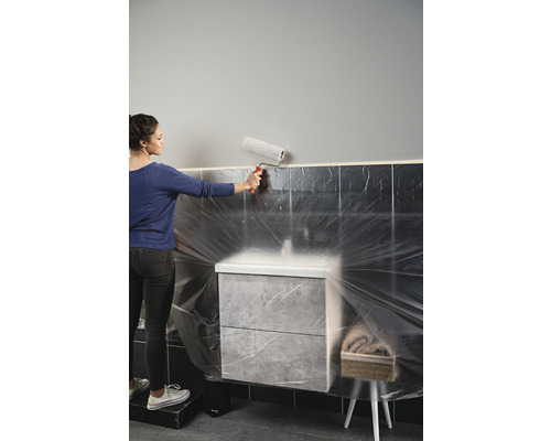 Femeie care vopsește un perete cu o rolă de vopsea într-o baie cu dulap de bază pentru chiuvetă