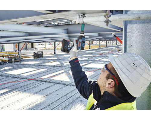 Un muncitor în construcții folosește o cheie de impact fără fir pe un șantier.