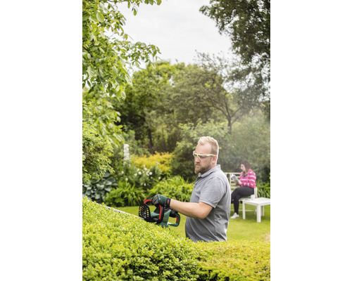 Un bărbat taie un gard viu cu o foarfecă de gard viu în grădină.