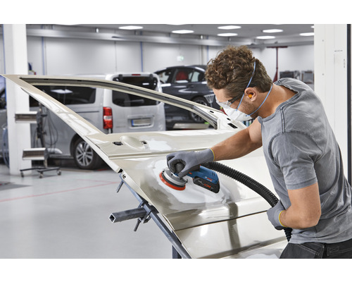 Un bărbat șlefuiește o ușă de mașină cu o mașină de șlefuit într-un atelier.