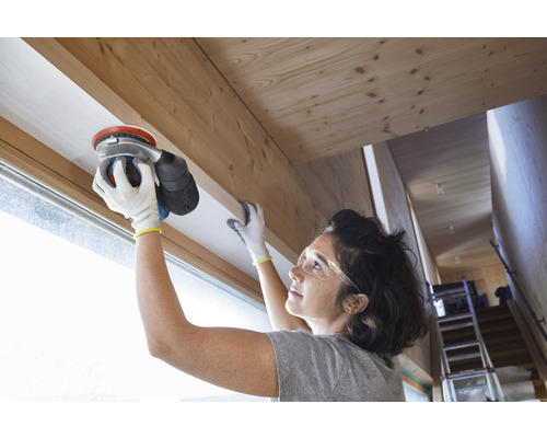 O femeie șlefuiește un cadru de fereastră din lemn cu o șlefuitoare excentrică.