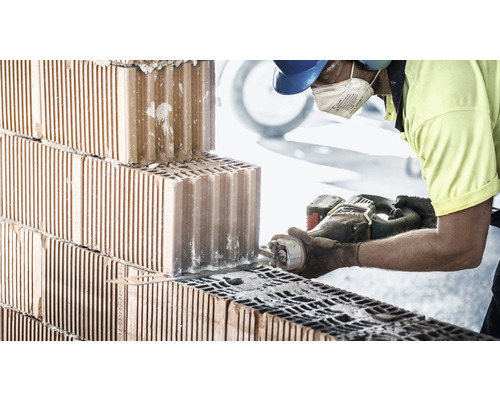 Un muncitor în construcții taie o cărămidă cu un ferăstrău.