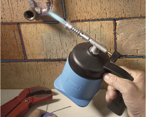 O mână folosește o torță pentru a lipi țevi pe un zid de cărămidă.