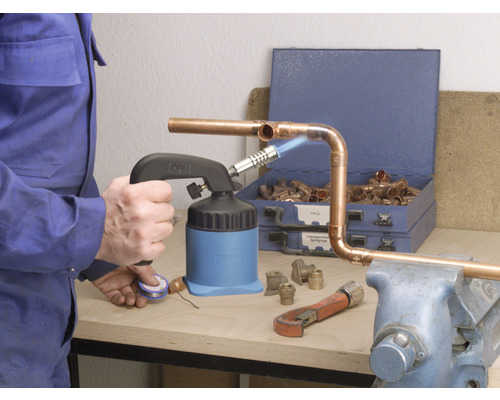 Artizan care sudează țevi de cupru cu un arzător de lipit, clești de țeavă și fitinguri de cupru pe un banc de lucru