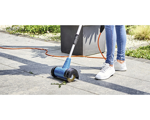 O persoană folosește o perie electrică pentru rosturi pe pavaj în grădină.