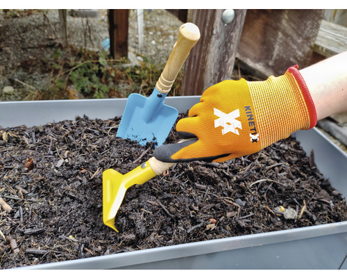 Imagine cu o mână în mănuși de grădinărit, un plivitor galben și o lopată albastră într-o jardinieră cu pământ.