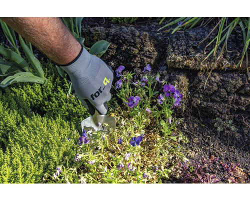 O persoană cu mănuși de grădinărit lucrează cu o plantatoare într-un strat de grădină.