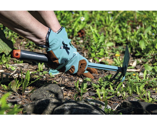 Persoană îndepărtând buruienile cu o sapă de grădină și purtând mănuși de grădinărit.