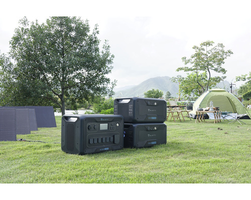 Scenă cu centrale electrice portabile Bluetti, panouri solare și un cort pe un gazon.