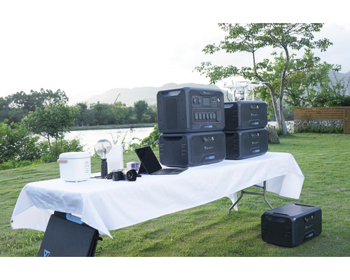 Imagine cu o scenă exterioară cu mai multe centrale electrice portabile Bluetti pe o masă, împreună cu diverse dispozitive