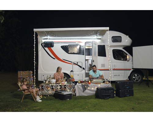Familie se bucură de o vacanță cu campingul în fața unei rulote cu luminițe și un generator solar