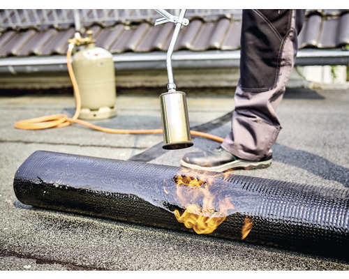 Un instalator de acoperișuri sudează o membrană bituminoasă cu un arzător cu gaz pe un acoperiș.