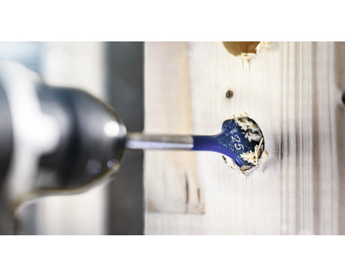 Un burghiu plat face o gaură într-o scândură de lemn cu o șurubelniță fără fir