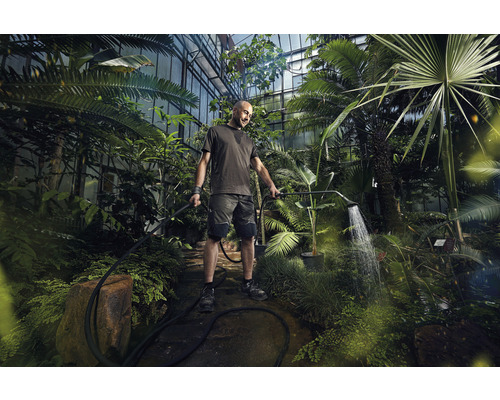 Un bărbat udă plantele într-o seră cu un duș de grădină.