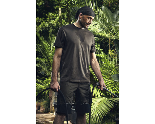 Un bărbat în haine de lucru ține un furtun de grădină într-o grădină.